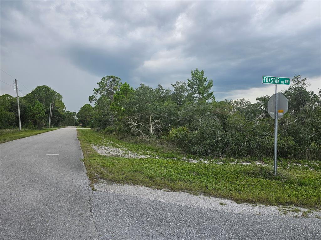 A paved road leads to a vacant, wooded lot at a street corner with signage — 643 BUCCANEER STREET NW, LAKE PLACID, FL