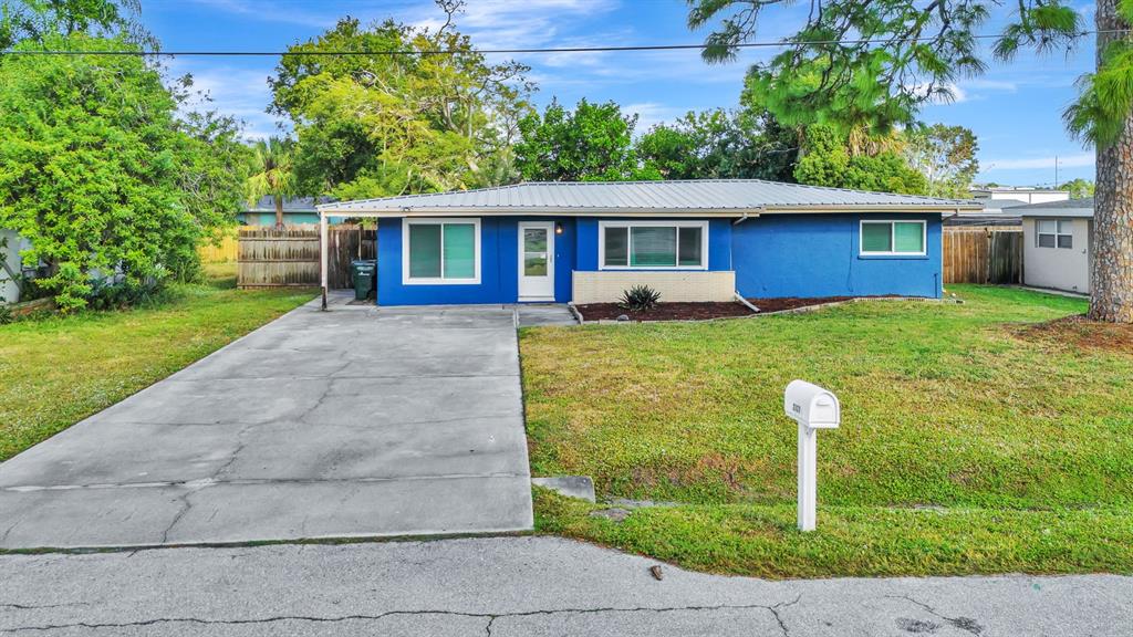 A single-story blue house with a metal roof, concrete driveway, and front lawn — 2127 LEE LANE, SARASOTA, FL