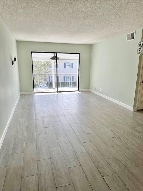 An empty living room features light wood-look tile flooring, pale green walls, and a sliding door — 130 Cypress Club Drive Apt 323, Pompano Beach FL 33060, POMPANO BEACH, FL