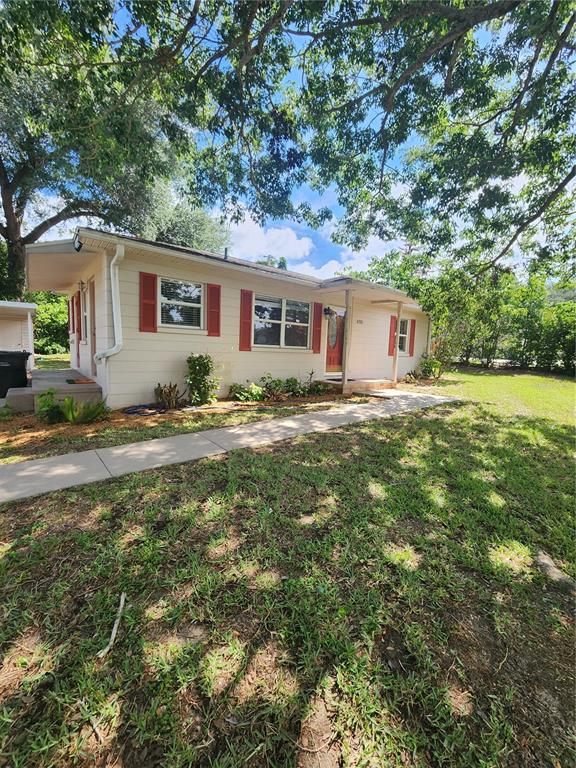 A single-story house with light siding, red shutters, and a concrete walkway under large trees — 4320 HEDGE DRIVE N, LAKELAND, FL