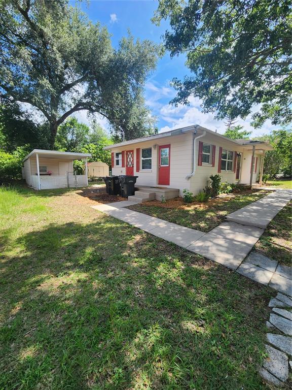 A single-story house with light siding, red doors, and a detached carport in a yard — 4320 HEDGE DRIVE N, LAKELAND, FL
