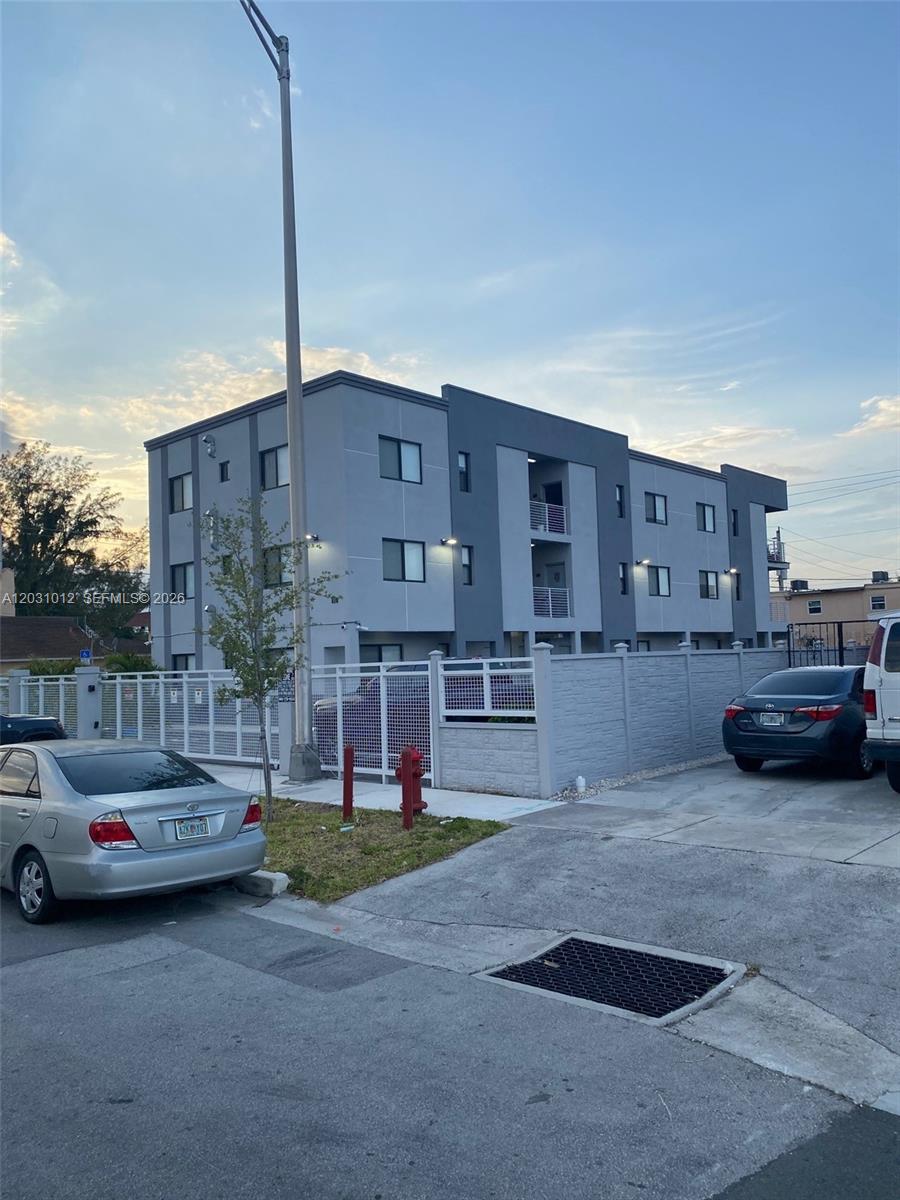 A three-story apartment building with a gray facade stands behind a white fence — 423 E 27th St # 302, Hialeah FL 33013, HIALEAH, FL