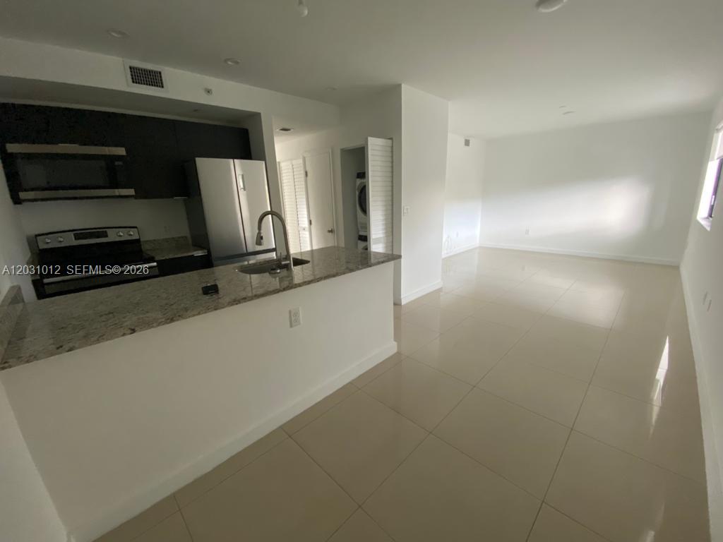 A kitchen with granite countertops and stainless steel appliances opens into a tiled living area — 423 E 27th St # 302, Hialeah FL 33013, HIALEAH, FL