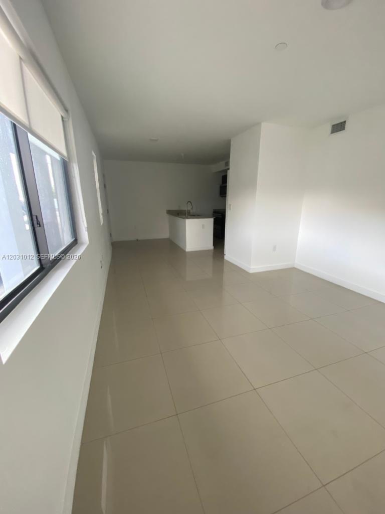 An open-concept living area with light tile flooring leads to a kitchen with white cabinets — 423 E 27th St # 302, Hialeah FL 33013, HIALEAH, FL