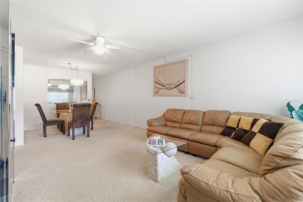A living room and dining area with beige carpet, a tan leather sectional, and ceiling fans — 2386 SUMATRAN WAY UNIT 14, CLEARWATER, FL