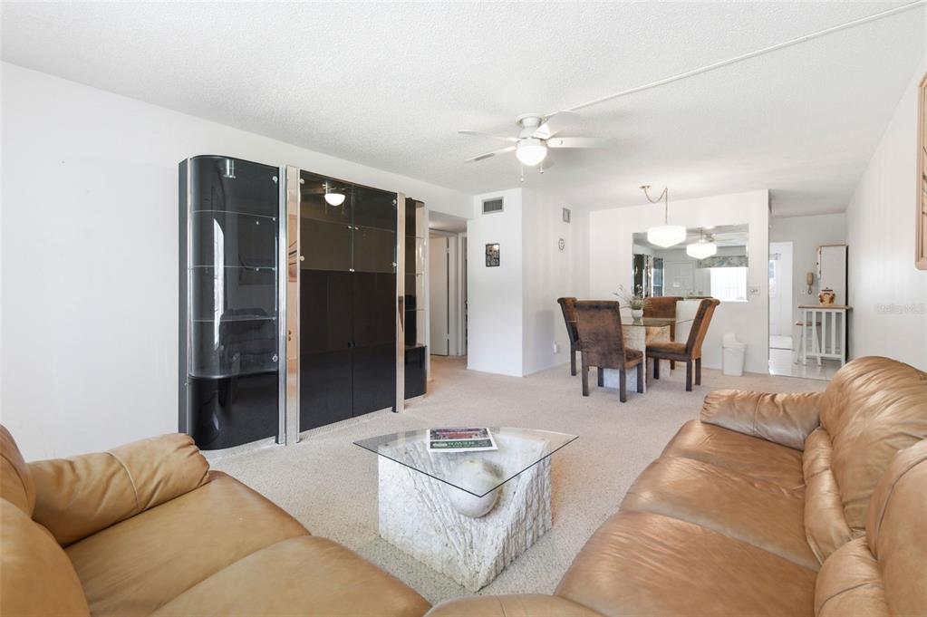 A living room and dining area featuring tan leather sofas, a glass coffee table, and cabinetry — 2386 SUMATRAN WAY UNIT 14, CLEARWATER, FL