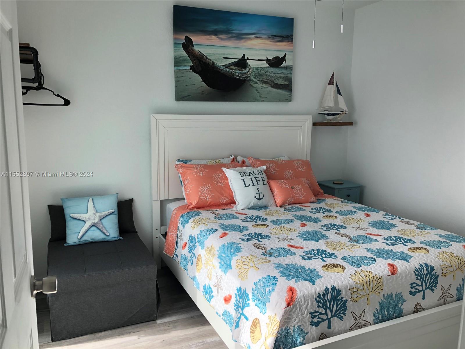 A bedroom features a bed with coral-patterned bedding, a gray ottoman, and nautical-themed wall art — 10877 Overseas Hwy # 38, Marathon FL 33050, MARATHON, FL