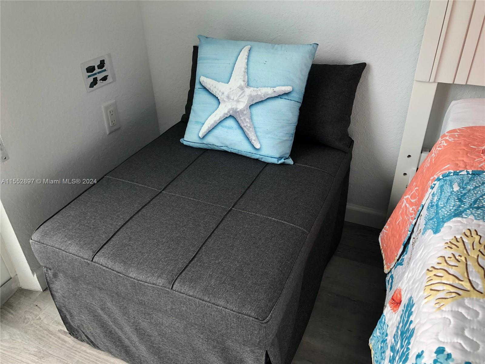 A grey upholstered ottoman with a starfish pillow sits next to a bed — 10877 Overseas Hwy # 38, Marathon FL 33050, MARATHON, FL