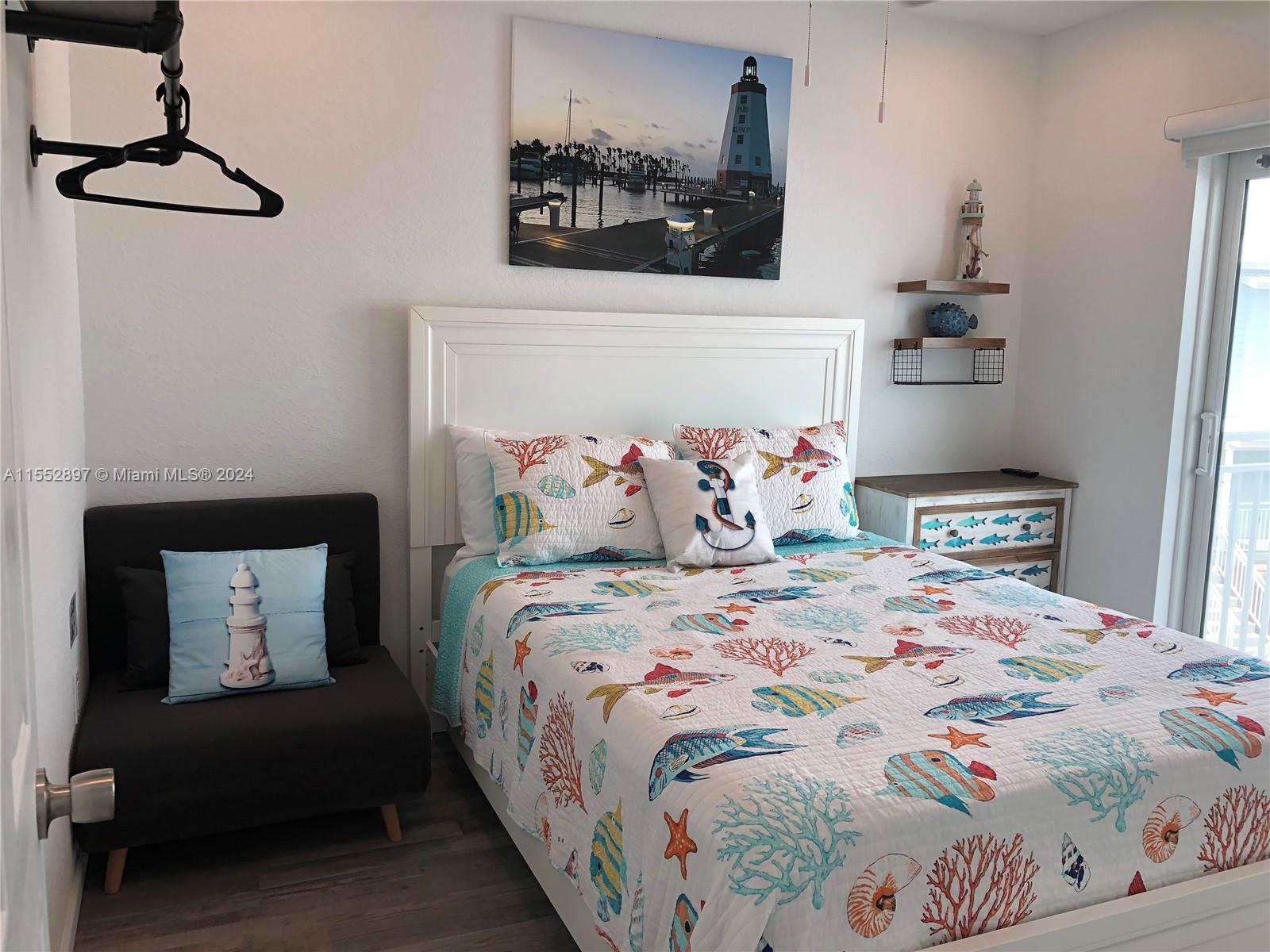 A bedroom features a nautical-themed quilt, a lighthouse print, and a dark gray accent chair — 10877 Overseas Hwy # 38, Marathon FL 33050, MARATHON, FL