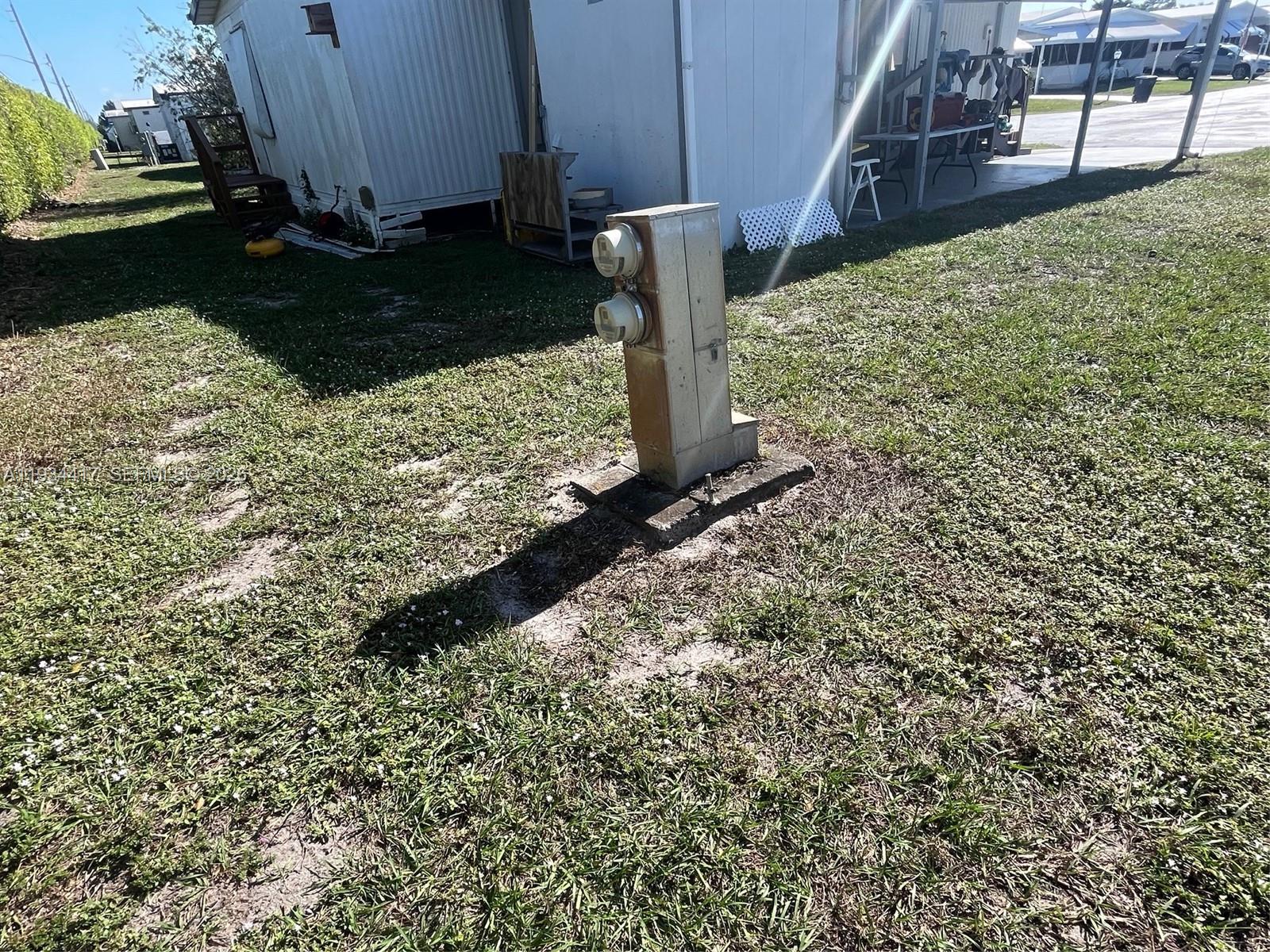 An outdoor electrical pedestal with two meters stands on a concrete pad in a yard — 56007 Amparo Bay, Boynton Beach FL 33436, BOYNTON BEACH, FL