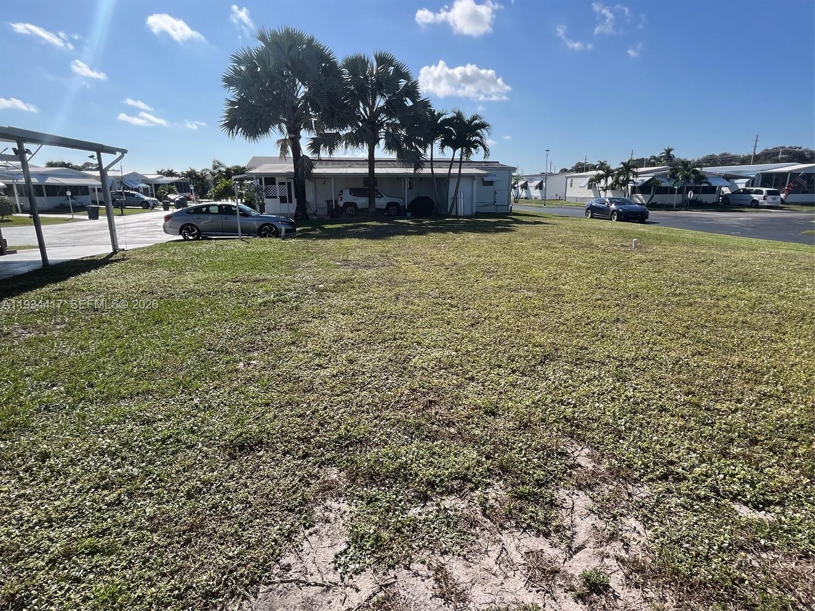 A grassy vacant lot sits in front of a mobile home with palm trees — 56007 Amparo Bay, Boynton Beach FL 33436, BOYNTON BEACH, FL
