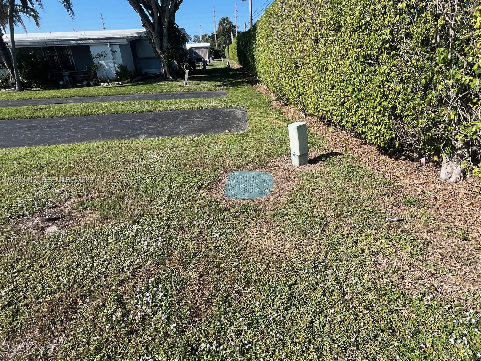 A grassy yard features a utility box and a green access cover near a hedge — 56007 Amparo Bay, Boynton Beach FL 33436, BOYNTON BEACH, FL