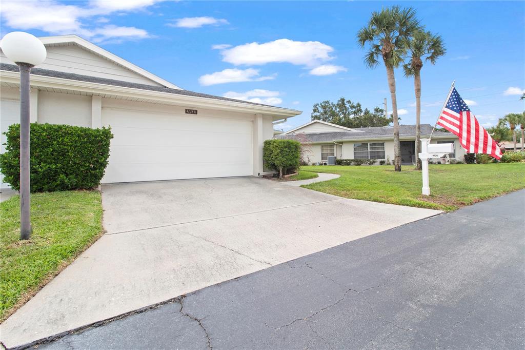 A single-story house with a white garage door, a concrete driveway, and an American flag — 4136 BOWLING GREEN CIRCLE UNIT 23, SARASOTA, FL
