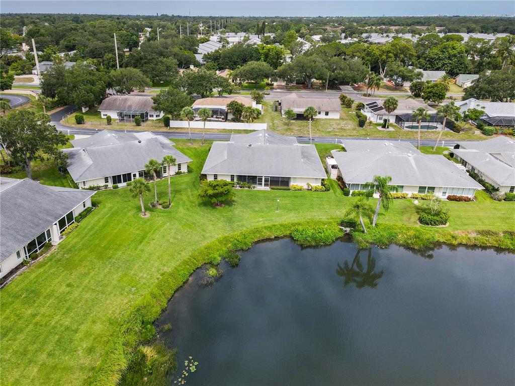 An aerial view shows several residential buildings with gray roofs surrounding a small pond — 4136 BOWLING GREEN CIRCLE UNIT 23, SARASOTA, FL