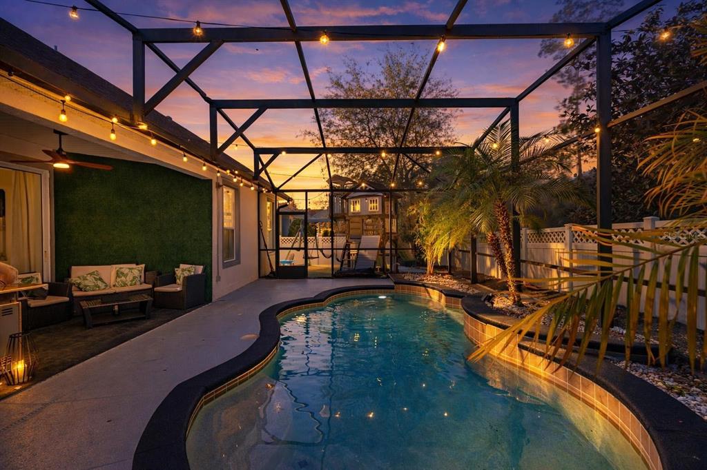 A screened-in patio features a curved swimming pool, palm tree, and outdoor seating area at sunset — 400 BROOKFIELD TERRACE, DELAND, FL
