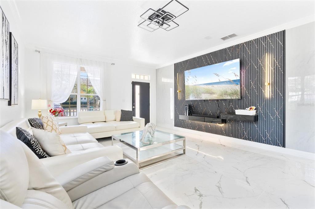 A bright living room features white leather sofas, a glass coffee table, and a slatted wall — 400 BROOKFIELD TERRACE, DELAND, FL