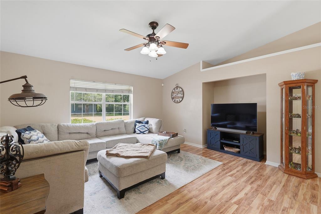A living room features a sectional sofa, a television on a blue console, and wood flooring — 18145 NW 250TH TERRACE, HIGH SPRINGS, FL