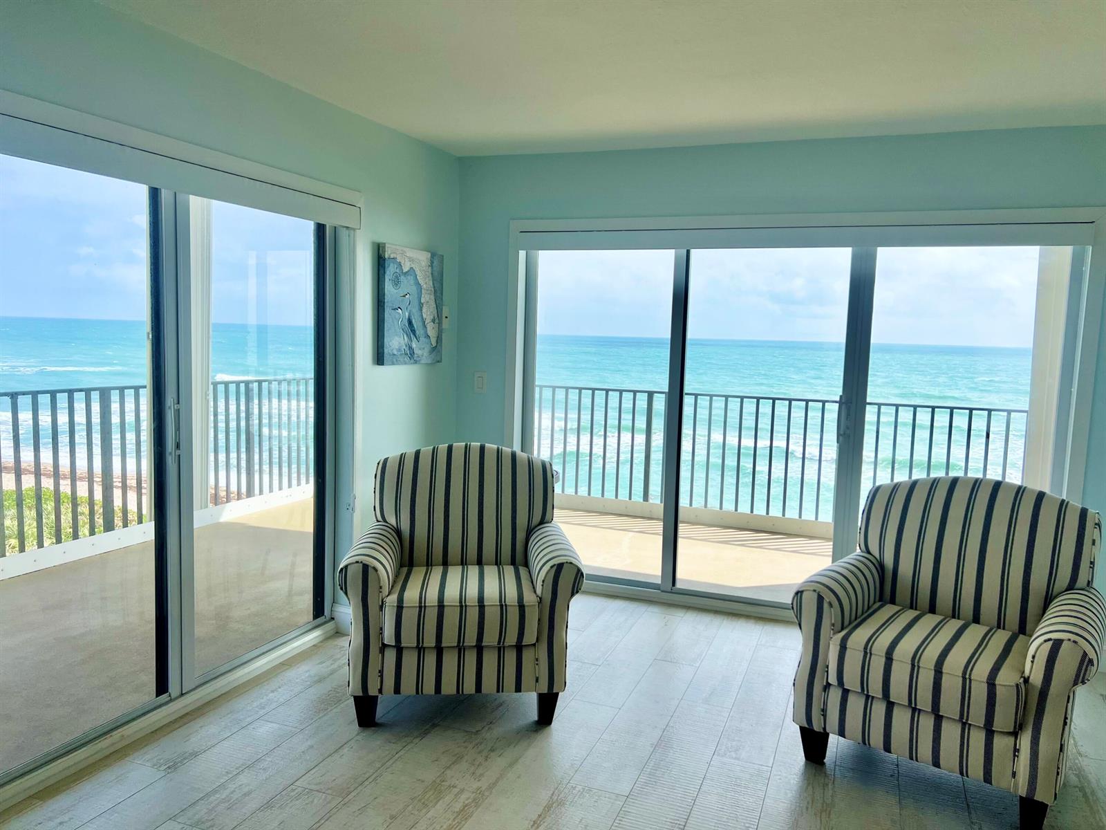 Two striped armchairs sit in a room with light wood floors and large sliding glass doors — 7410 S Ocean Drive # 505, Jensen Beach FL 34957, JENSEN BEACH, FL