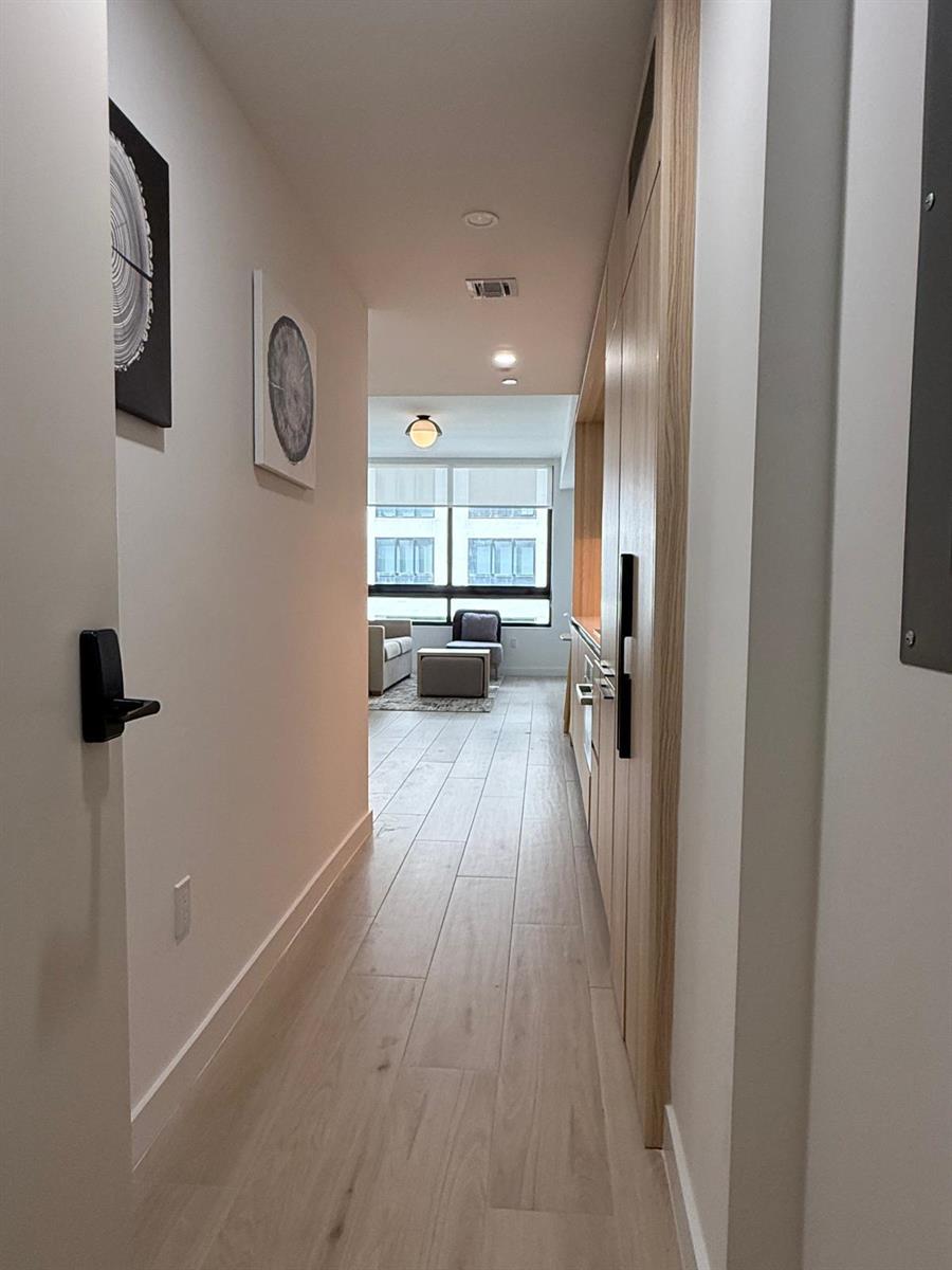 A hallway with light wood flooring leads to a living area with large windows — 225 N Miami Avenue # 804, Miami FL 33128, MIAMI, FL