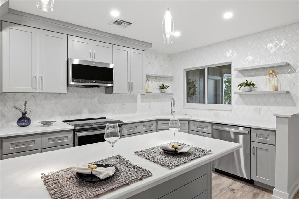 A modern kitchen features gray cabinets, white quartz countertops, a tiled backsplash, and a central island — 6030 BOCA GRANDE CAUSEWAY UNIT B21, BOCA GRANDE, FL