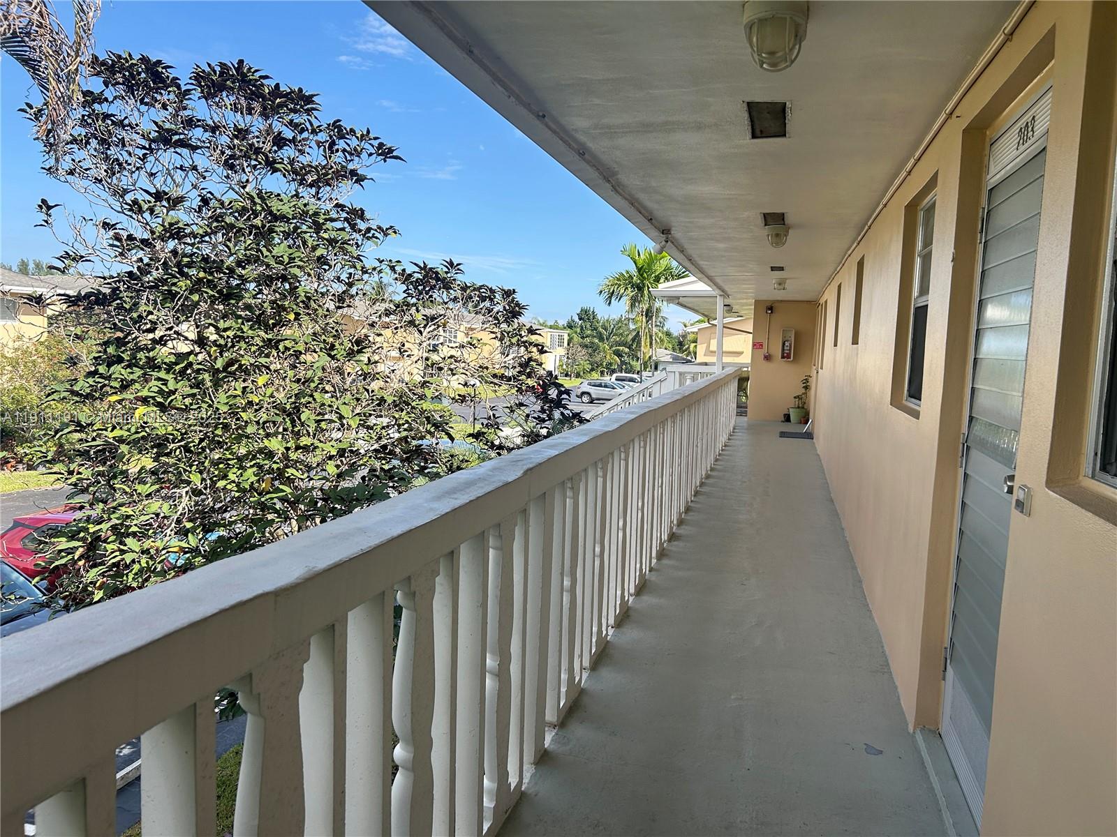 An outdoor apartment balcony with a white railing overlooks a parking lot and trees — 2112 NE 1st Way # 203, Boynton Beach FL 33435, BOYNTON BEACH, FL