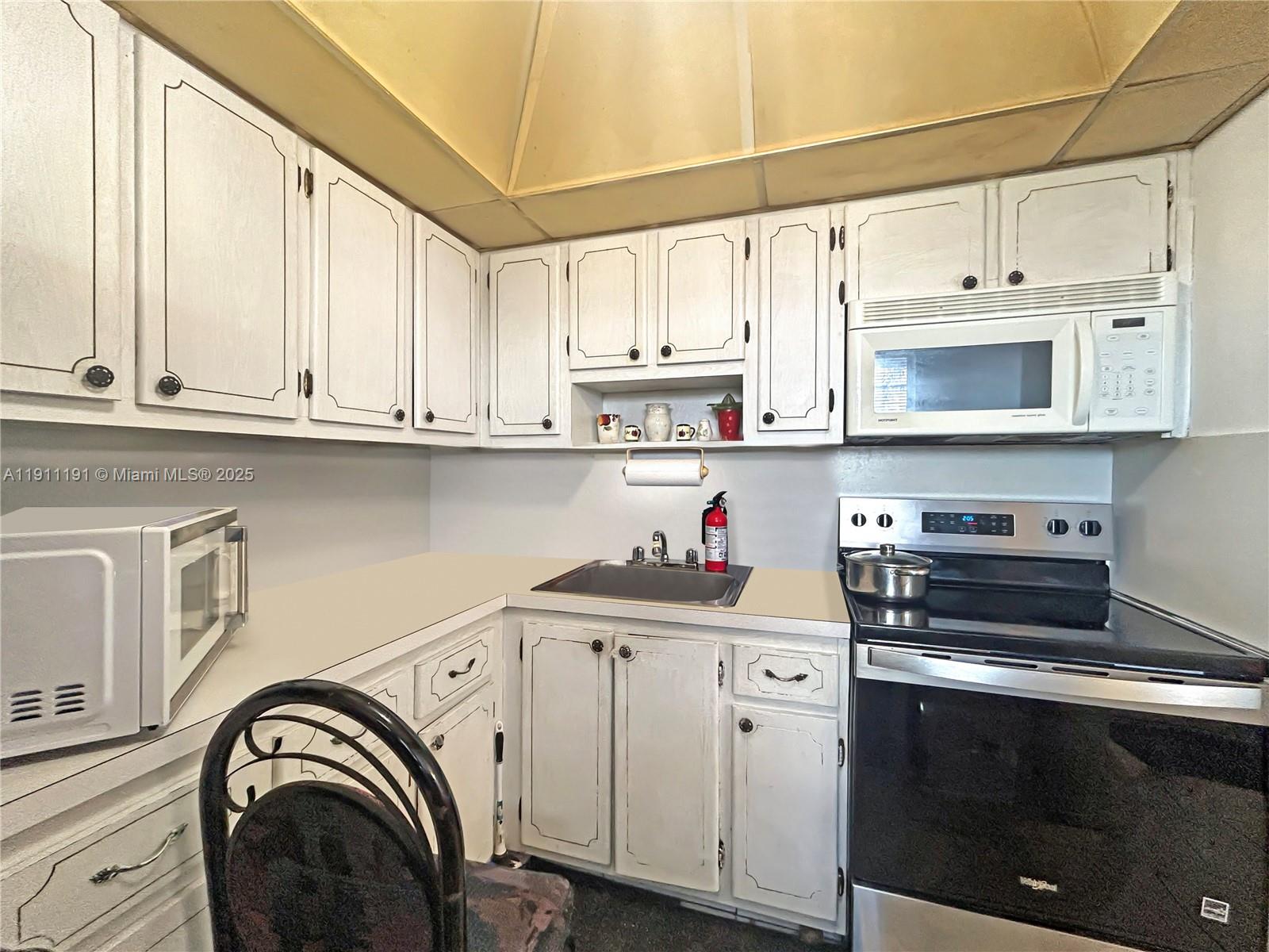 A small kitchen features white cabinets, a stainless steel sink, and black appliances — 2112 NE 1st Way # 203, Boynton Beach FL 33435, BOYNTON BEACH, FL