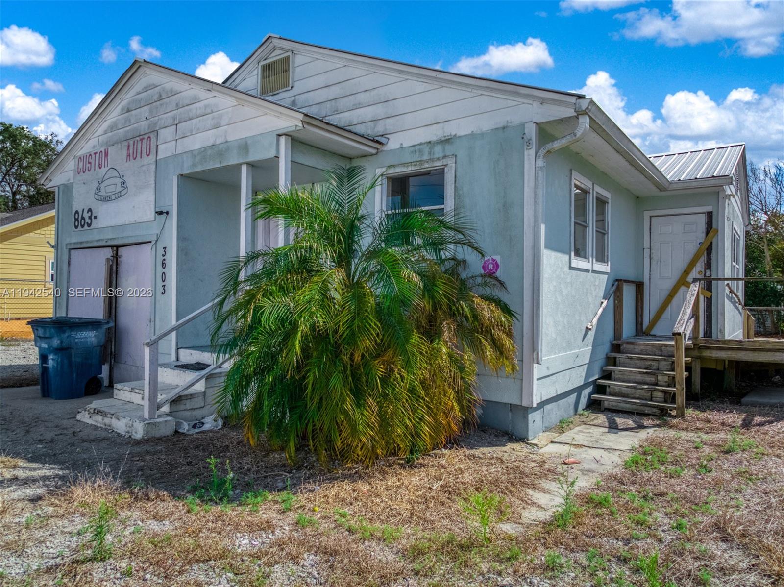 A weathered, light-colored commercial building with a palm tree in front and wooden stairs — 3603 Kenilworth Blvd, Sebring FL 33870, SEBRING, FL