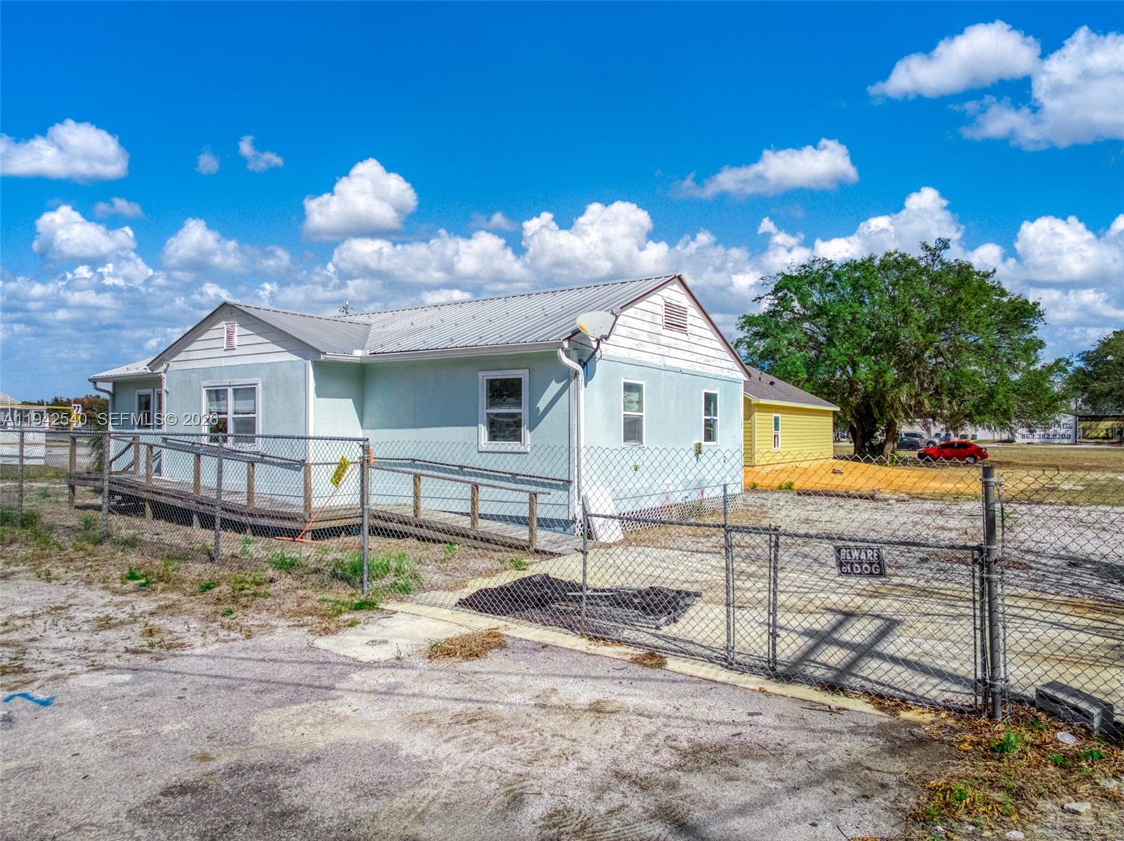A light blue house with a metal roof and a wooden wheelchair ramp sits behind fencing — 3603 Kenilworth Blvd, Sebring FL 33870, SEBRING, FL