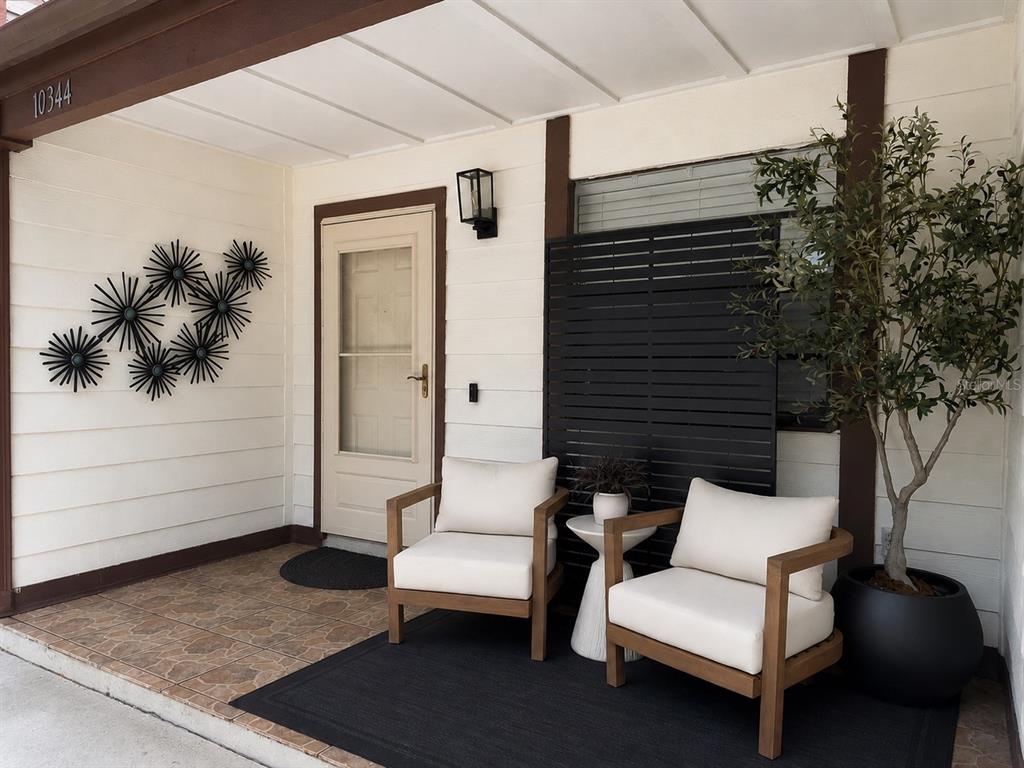 A covered porch features two wooden chairs with white cushions, a black privacy screen, and decor — 10344 COUNCILS WAY, TAMPA, FL