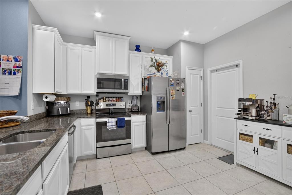 A kitchen with white cabinets, stainless steel appliances, granite countertops, and light tile flooring — 2911 JACOB CROSSING LANE, HOLIDAY, FL