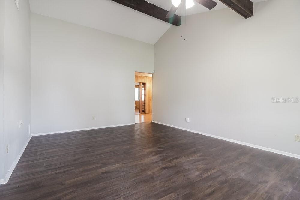 An empty room with vaulted ceilings, dark wood-look flooring, and a ceiling fan — 123 HIDALGO AVENUE, KISSIMMEE, FL