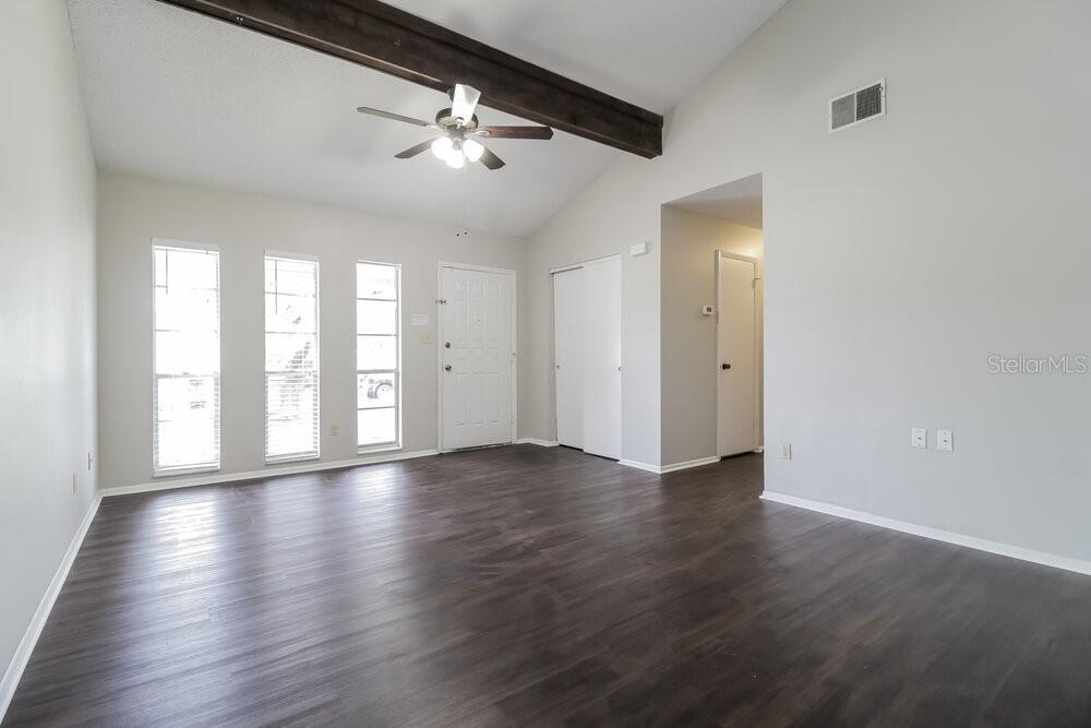 A living room with dark wood-look flooring, a vaulted ceiling, and a wooden ceiling beam — 123 HIDALGO AVENUE, KISSIMMEE, FL