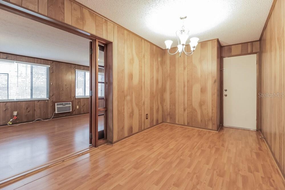 A dining room features wood-paneled walls, light wood flooring, and a white chandelier — 123 HIDALGO AVENUE, KISSIMMEE, FL