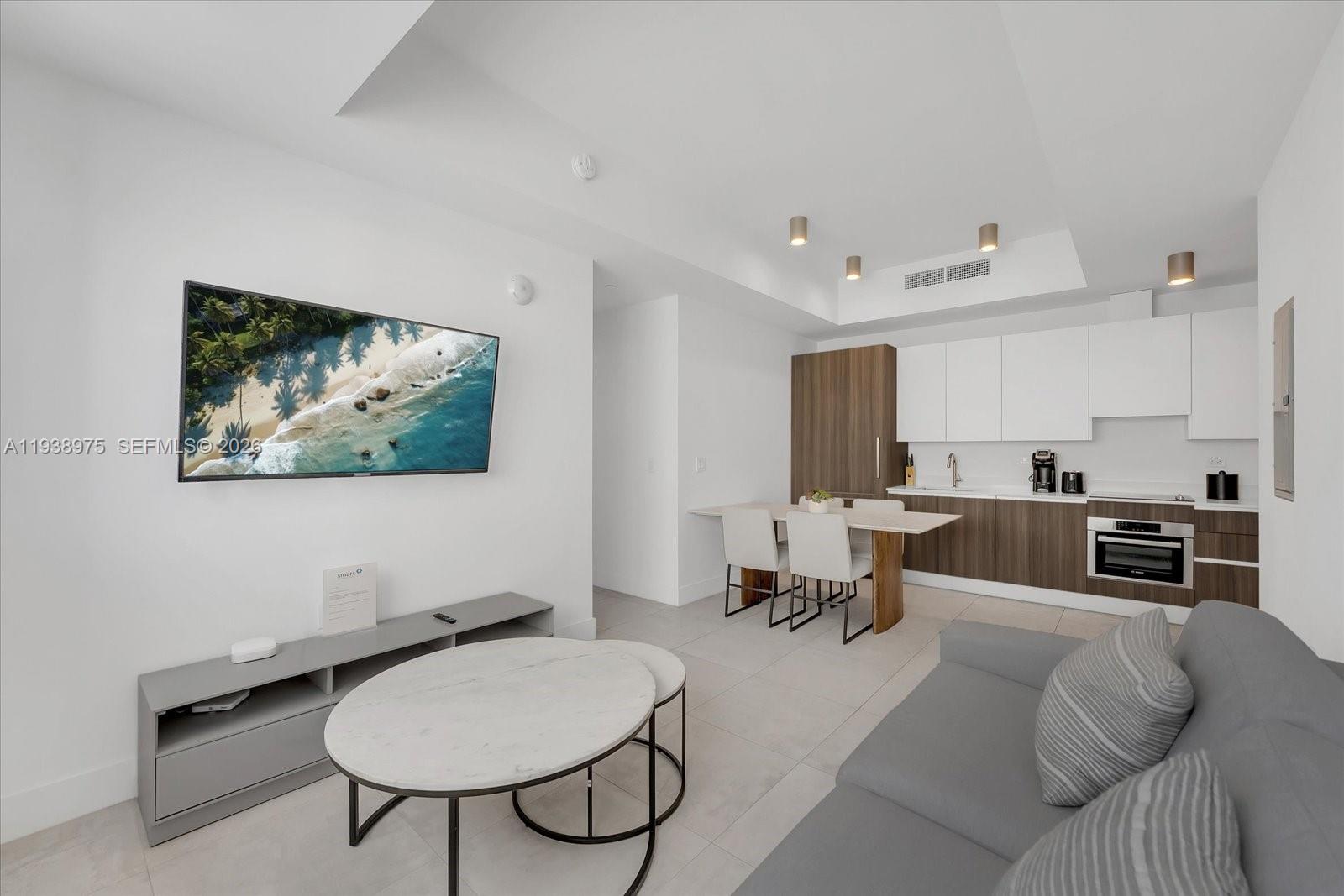 A modern living room and kitchen area feature white walls, light tile floors, and wood cabinetry — 239 SW 9th St # 1603, Miami FL 33130, MIAMI, FL
