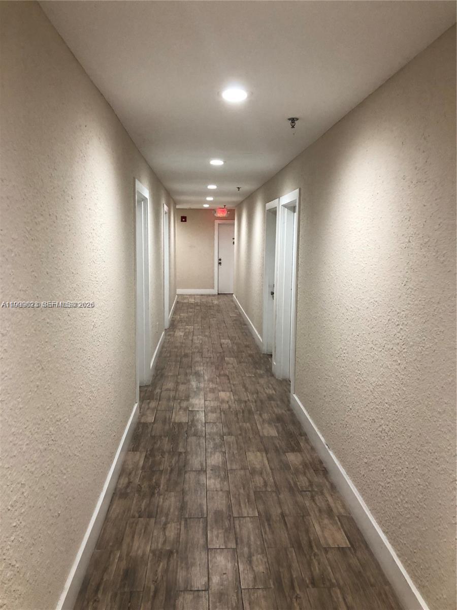 A long, narrow hallway features light-colored walls, recessed ceiling lights, and wood-look tile flooring — 2730 Collins Ave # 310, Miami Beach FL 33140, MIAMI BEACH, FL