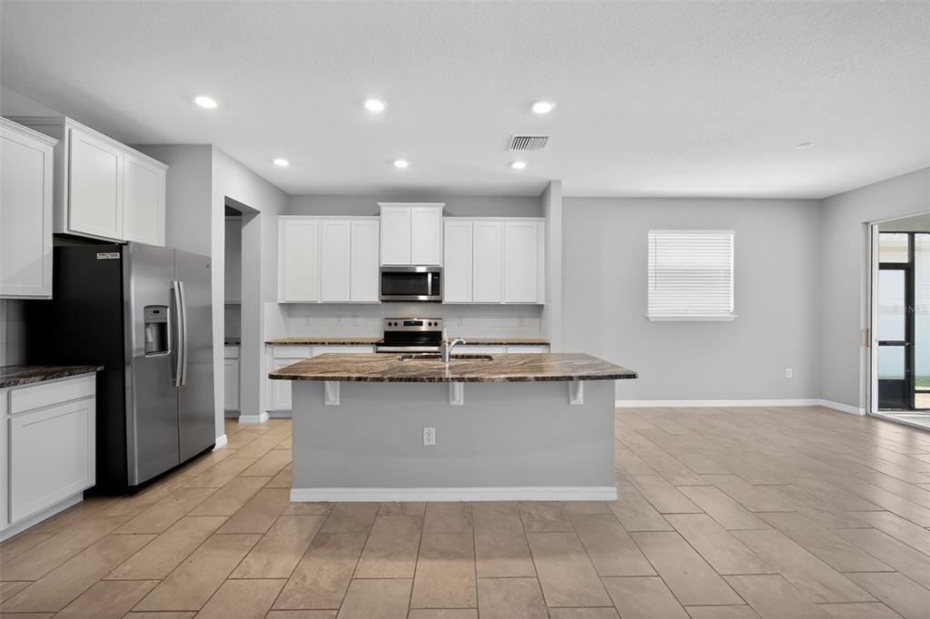 A kitchen with white cabinets, stainless steel appliances, a granite island, and tiled flooring — 15394 SWEET SPRINGS BEND, ODESSA, FL