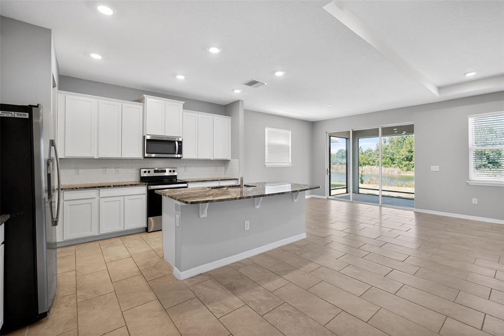 A kitchen with white cabinets, a granite island, and tile flooring opens to a patio — 15394 SWEET SPRINGS BEND, ODESSA, FL
