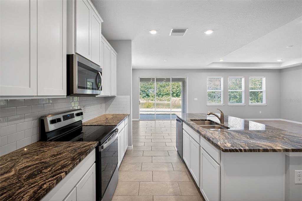 A kitchen features white cabinets, granite countertops, stainless steel appliances, and tile flooring — 15394 SWEET SPRINGS BEND, ODESSA, FL