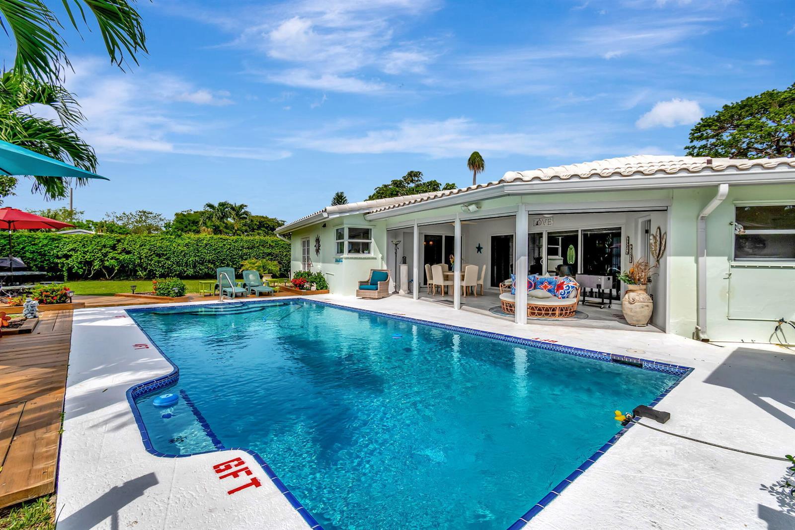 A backyard swimming pool sits in front of a light green house with a covered patio — 302 Venice Drive, Boynton Beach FL 33426, BOYNTON BEACH, FL