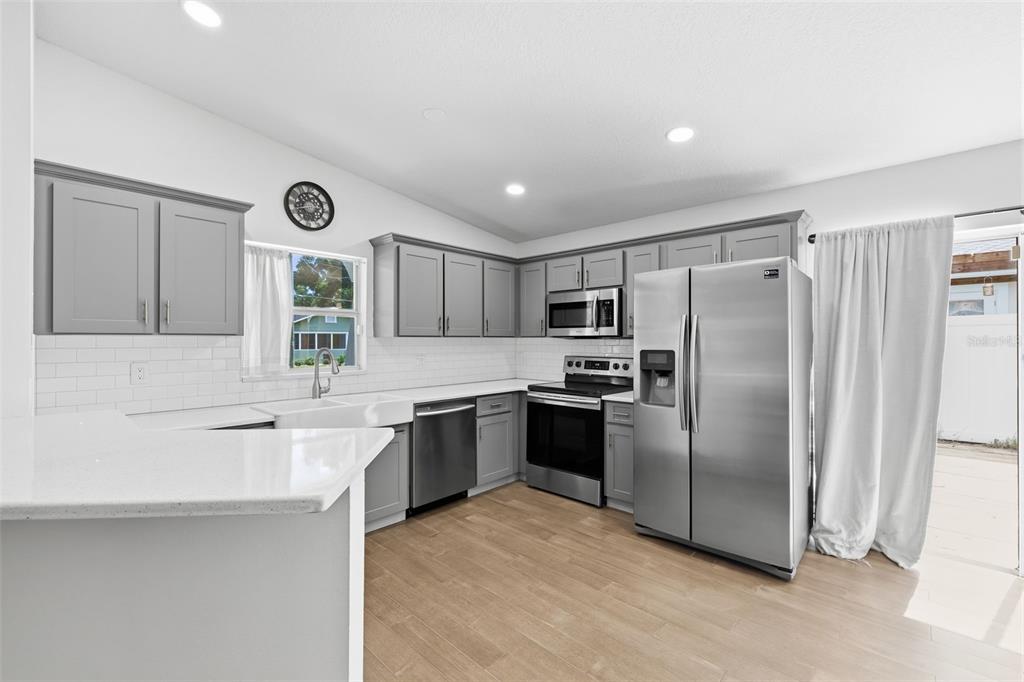 A kitchen with gray cabinets, stainless steel appliances, white countertops, and light wood-look flooring — 213 E CLUSTER AVENUE, TAMPA, FL