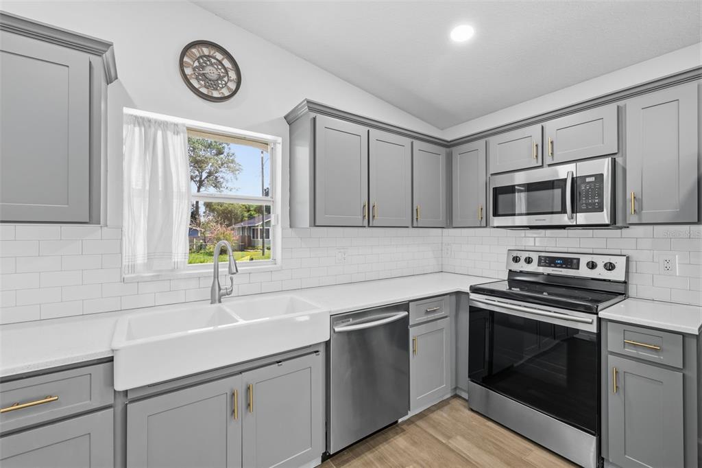 A kitchen features gray cabinets, white subway tile backsplash, stainless steel appliances, and a farmhouse sink — 213 E CLUSTER AVENUE, TAMPA, FL