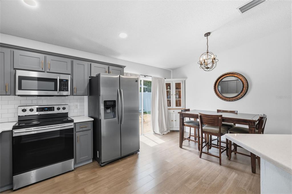 A kitchen with gray cabinets, stainless steel appliances, and a dining area with a round mirror — 213 E CLUSTER AVENUE, TAMPA, FL
