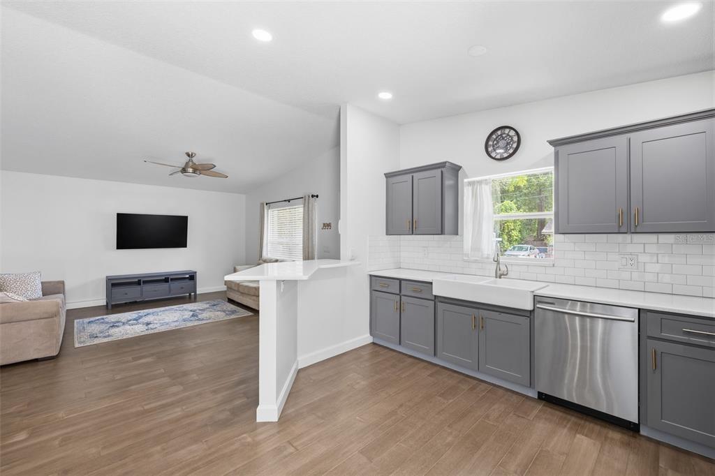 A kitchen with gray cabinets and a white farmhouse sink opens to a living area — 213 E CLUSTER AVENUE, TAMPA, FL
