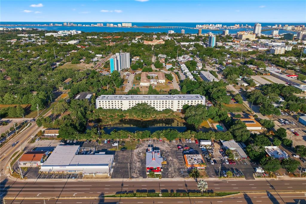 An aerial view shows a multi-story apartment building situated behind a commercial parking lot — 701 S MADISON AVENUE UNIT 420, CLEARWATER, FL