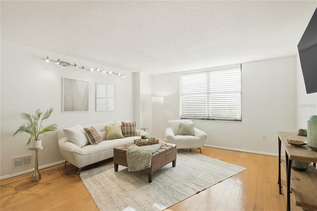 A living room features a white sofa, leather ottoman, armchair, and hardwood flooring — 701 S MADISON AVENUE UNIT 420, CLEARWATER, FL