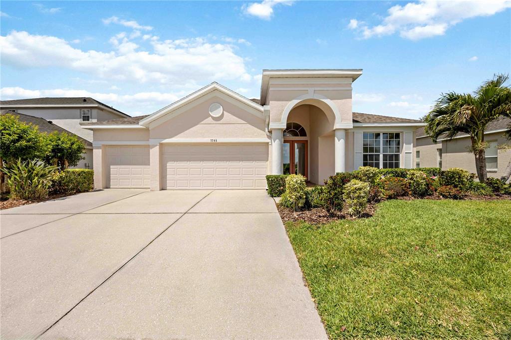 A single-story suburban house with a beige stucco exterior, three-car garage, and arched entryway — 7740 CASTLEISLAND DRIVE, SARASOTA, FL