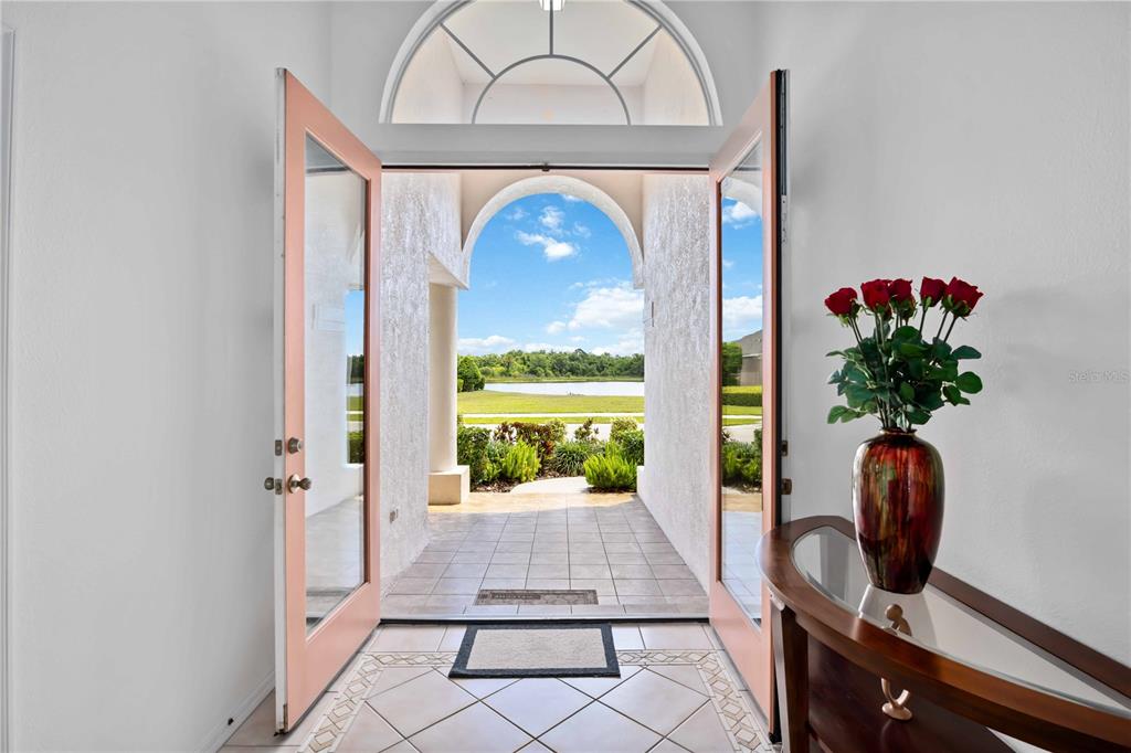An open doorway reveals a tiled entryway looking out toward a lake and green landscape — 7740 CASTLEISLAND DRIVE, SARASOTA, FL