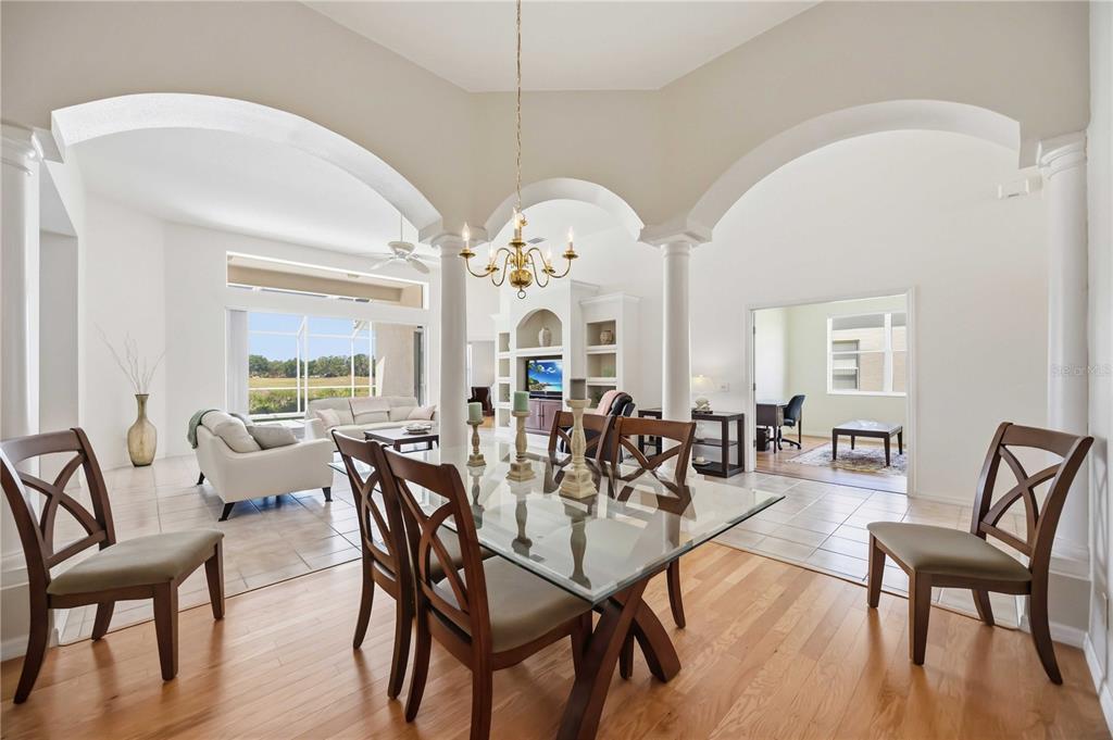 A dining room with a glass table and hardwood floors opens to a living area — 7740 CASTLEISLAND DRIVE, SARASOTA, FL