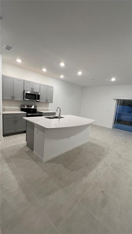 A modern kitchen features gray cabinets, stainless steel appliances, and a large white island — 5080 REVOLUTIONARY WAY, ST CLOUD, FL