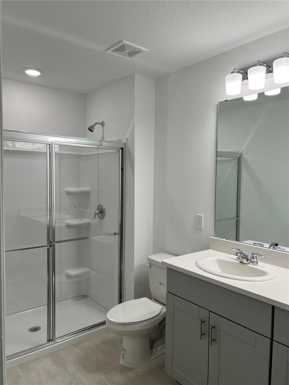 A bathroom features a glass-enclosed shower, a toilet, and a vanity with a gray cabinet — 5080 REVOLUTIONARY WAY, ST CLOUD, FL